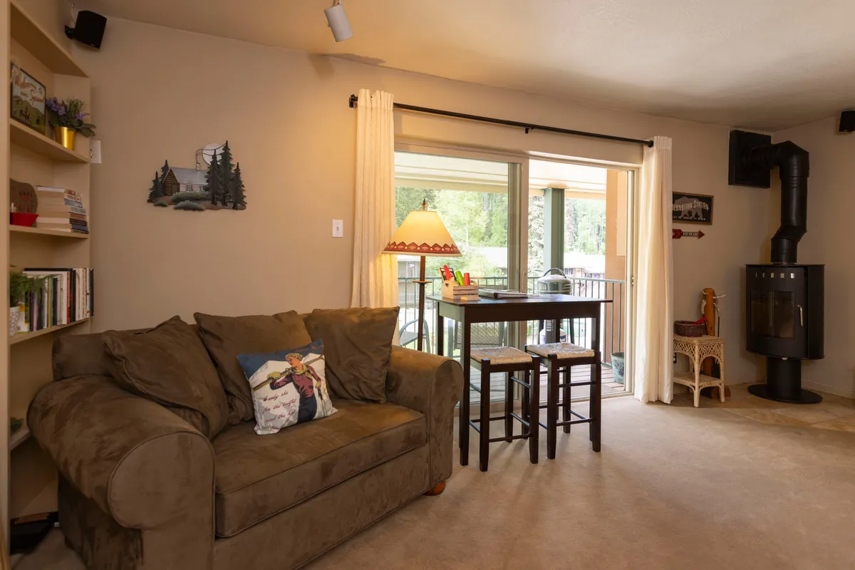 A cozy living area featuring a sofa, small table, lamp, and bookshelf, with subtle cues that suggest proximity to a balcony or large windows. The ambiance hints at relaxation after outdoor adventures and enjoying scenic views from the comfort of the condo.