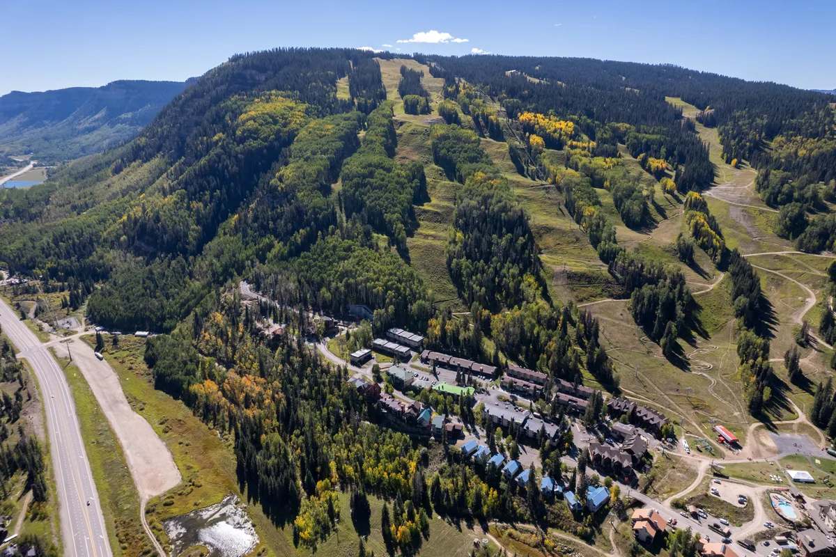 A wide, exterior view of the Purgatory Lodge area showcasing the majestic mountain slopes, dense forest, and residential buildings. The scene captures the spirit of adventure, as well as the tranquil beauty of the resort and its surrounding environment.