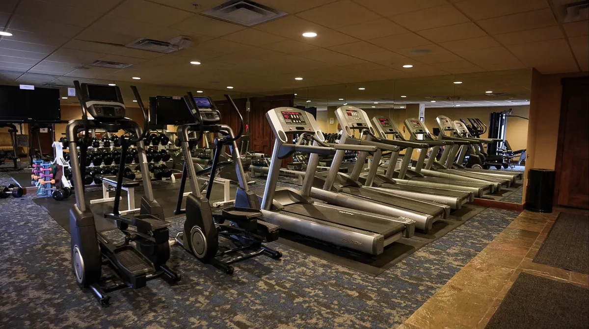 This image captures a vibrant fitness center with elliptical machines, treadmills, free weights, and television screens, all illuminated with energetic lighting. The setup is modern and welcoming for individual or group workouts.