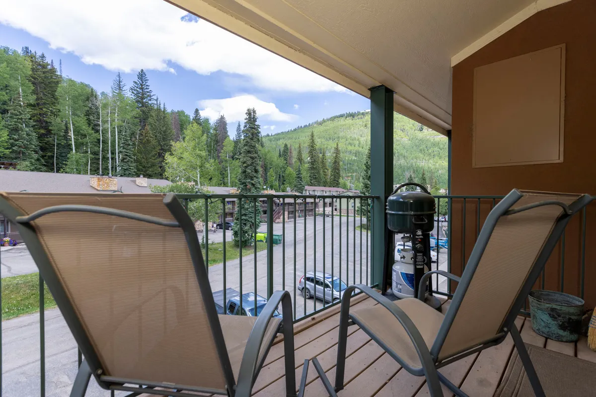 An exterior shot featuring a private balcony with comfortable chairs and a grill, looking out over breathtaking mountain scenery. The setting is serene and inviting, with the fresh mountain air and panoramic views providing a perfect spot for relaxation after outdoor activities.