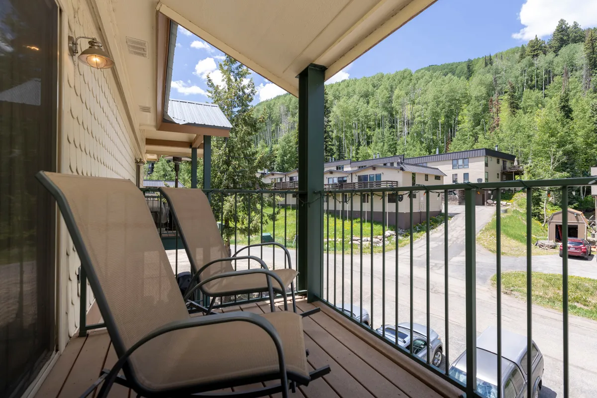 A tranquil balcony scene overlooking nearby buildings with expansive mountain views beyond. Balcony seating is visible, suggesting a relaxing vantage point to enjoy the landscape after a day of exploration.