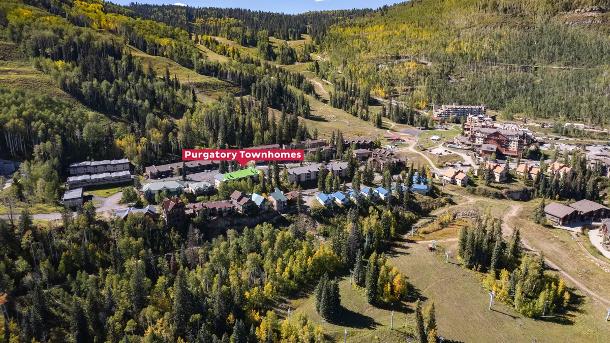 An inviting exterior scene showcasing the Purgatory Townhomes surrounded by lush forest and dramatic mountain slopes, emphasizing the connection to outdoor recreation and natural beauty.